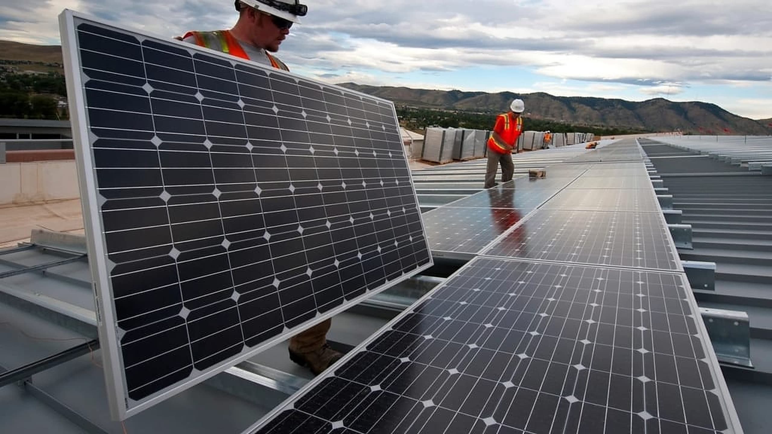Workers fitting solar panels on a low-slope commercial metal roof.